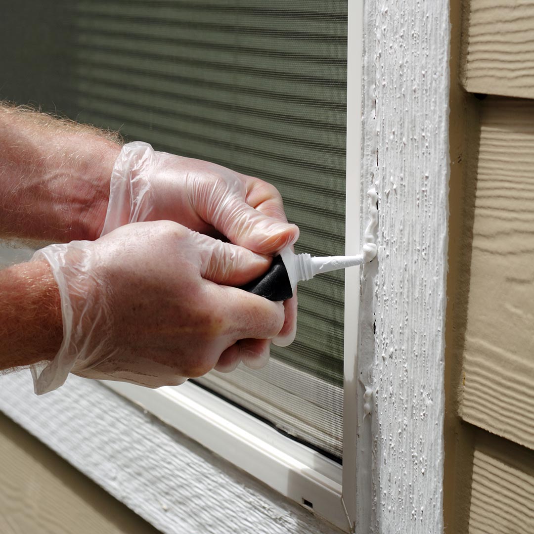 Man sealing up crack in wood around window