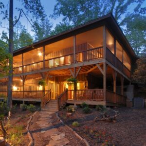 A two-story wooden home with large screened-in porches illuminated by warm interior lights at twilight.