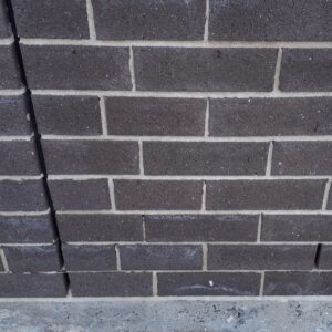A vertical crack running through the mortar and dark grey bricks of a wall.