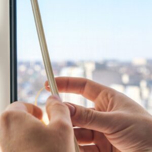 A pair of hands pressing a thin spline into the groove of a window screen frame.