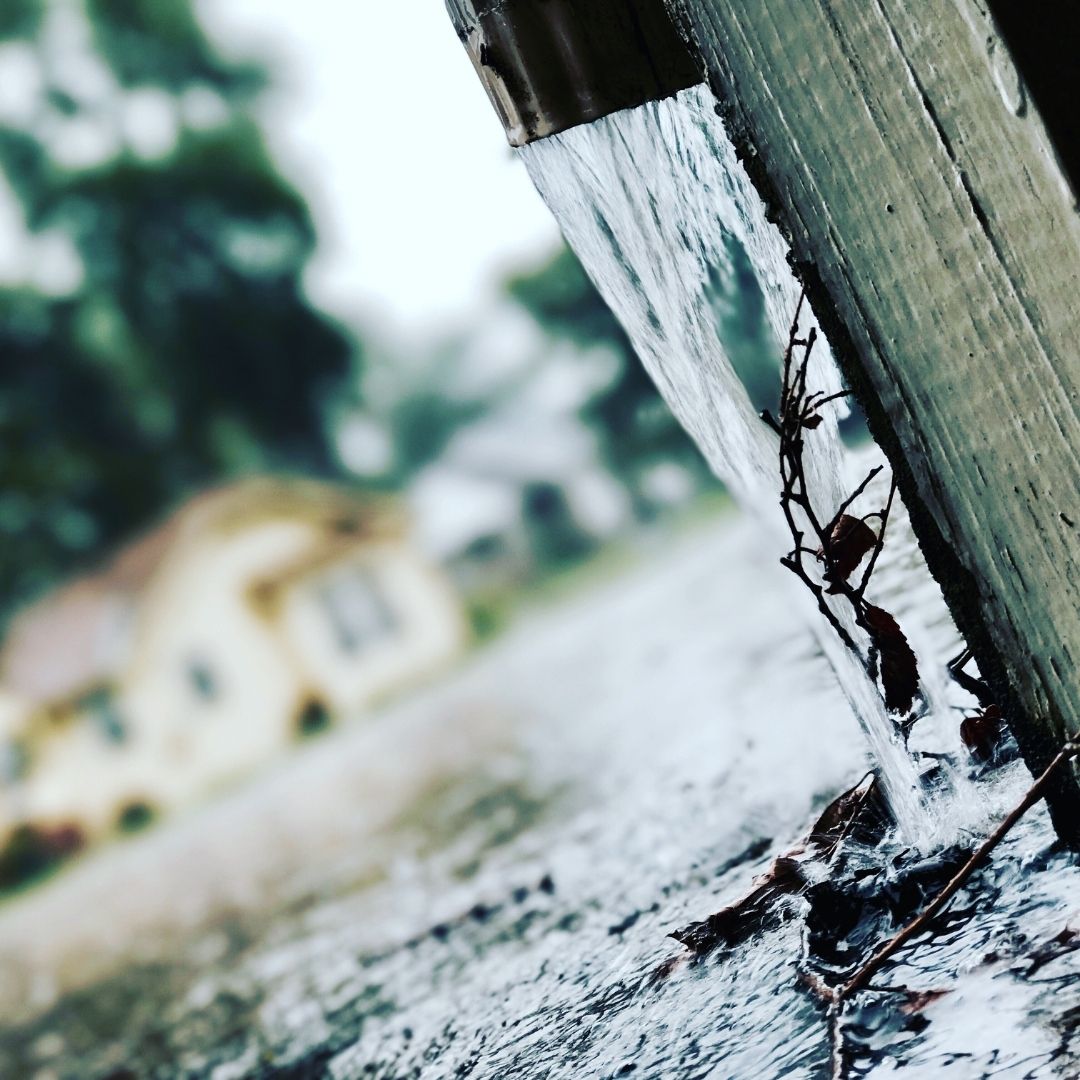 Downspout directing heavy rainwater away from a house foundation.